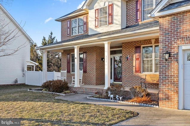 view of exterior entry featuring fence, a porch, and brick siding