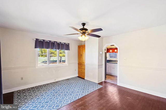 empty room featuring dark wood-style floors, arched walkways, baseboards, and a ceiling fan