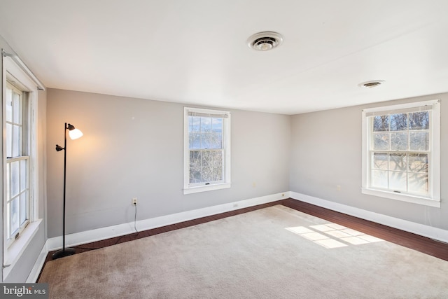 empty room featuring dark wood-style flooring, visible vents, and baseboards