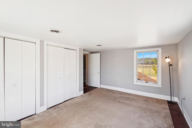 unfurnished bedroom featuring baseboards, carpet, visible vents, and multiple closets