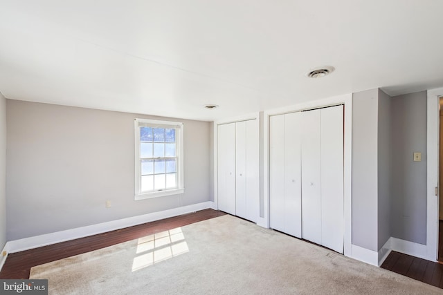 unfurnished bedroom featuring visible vents, dark wood finished floors, baseboards, and two closets