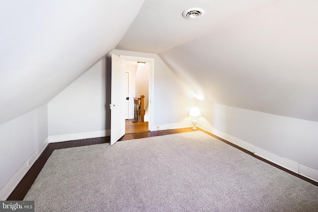 additional living space featuring dark wood finished floors, lofted ceiling, dark colored carpet, visible vents, and baseboards