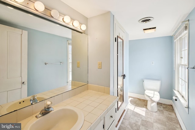 bathroom featuring toilet, vanity, visible vents, and a healthy amount of sunlight