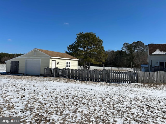 snow covered back of property with a fenced front yard and a detached garage