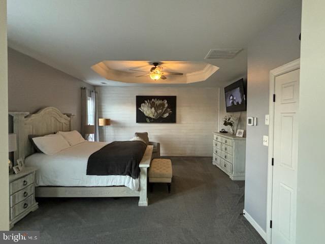 bedroom featuring dark carpet, a ceiling fan, a raised ceiling, and baseboards