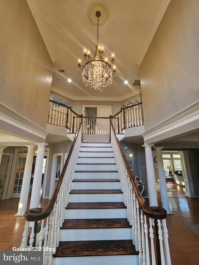 stairs with crown molding, a high ceiling, ornate columns, and wood finished floors