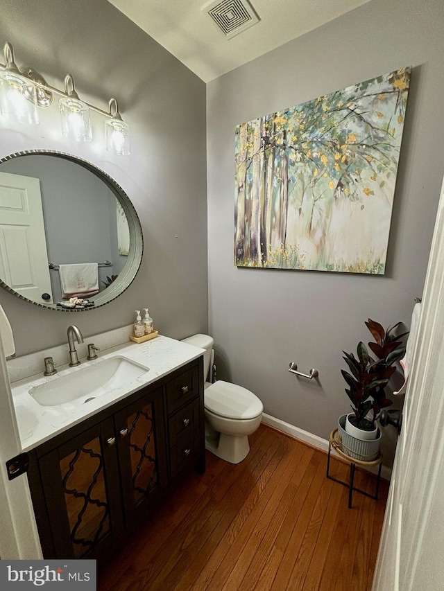 half bathroom with visible vents, toilet, wood-type flooring, baseboards, and vanity