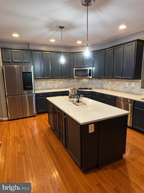 kitchen featuring light wood finished floors, a center island, light countertops, hanging light fixtures, and stainless steel appliances