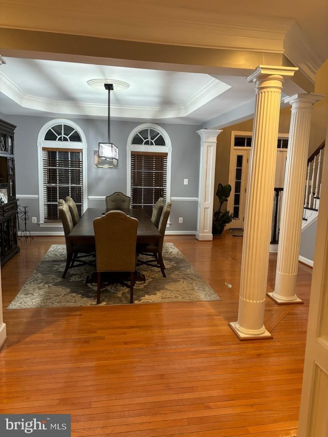 dining room with a raised ceiling, decorative columns, and wood finished floors