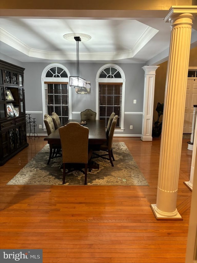 dining room with a raised ceiling, wood finished floors, ornamental molding, and ornate columns