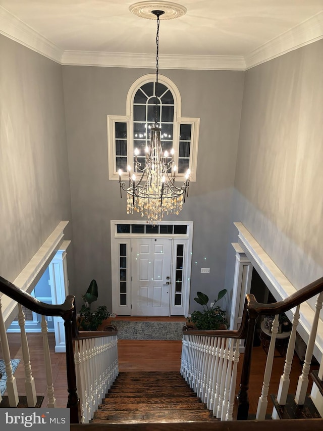 entryway with crown molding, stairs, an inviting chandelier, and wood finished floors