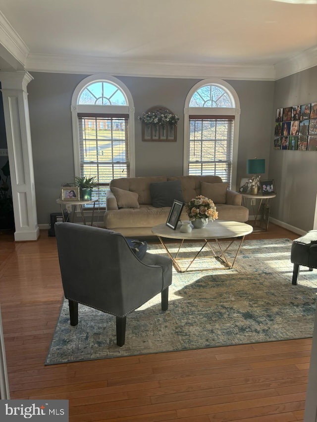 living area with decorative columns, wood finished floors, baseboards, and ornamental molding