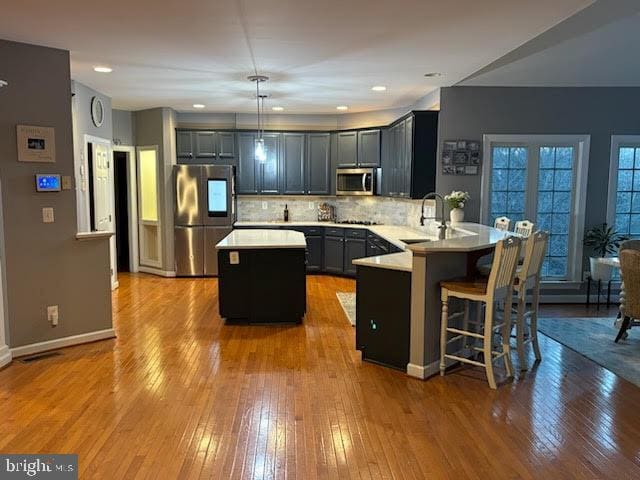 kitchen with backsplash, light countertops, a peninsula, stainless steel appliances, and a sink