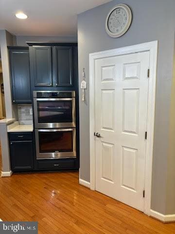 kitchen with light wood finished floors, stainless steel double oven, light countertops, and baseboards