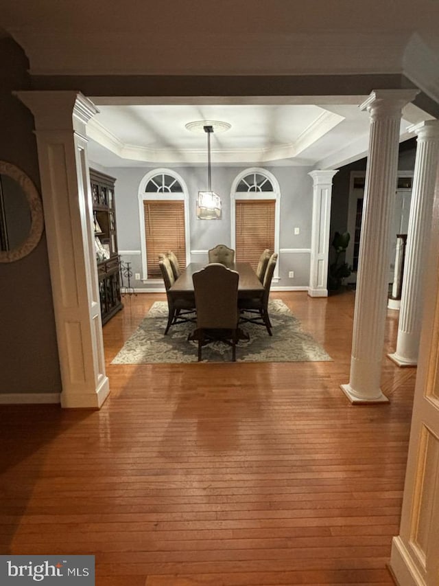 dining space with a tray ceiling, wood-type flooring, ornate columns, and ornamental molding