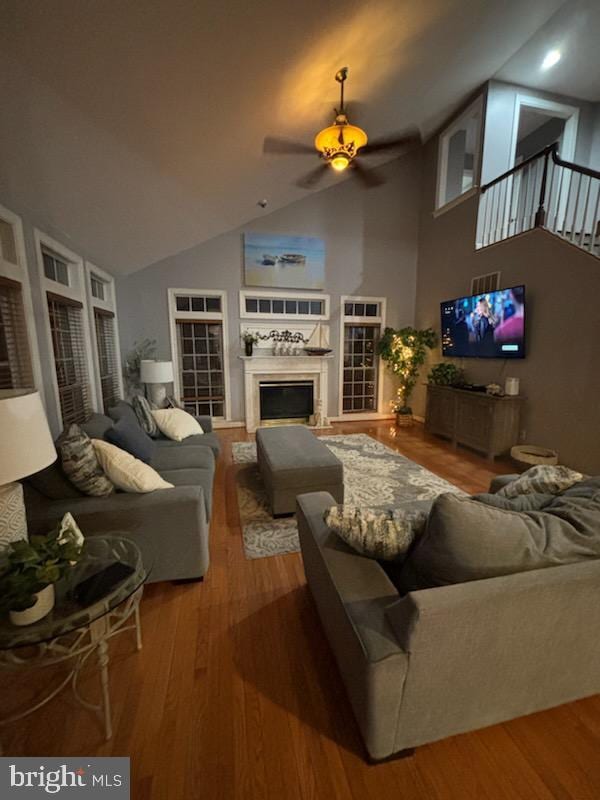 living room with a glass covered fireplace, high vaulted ceiling, a ceiling fan, and wood finished floors