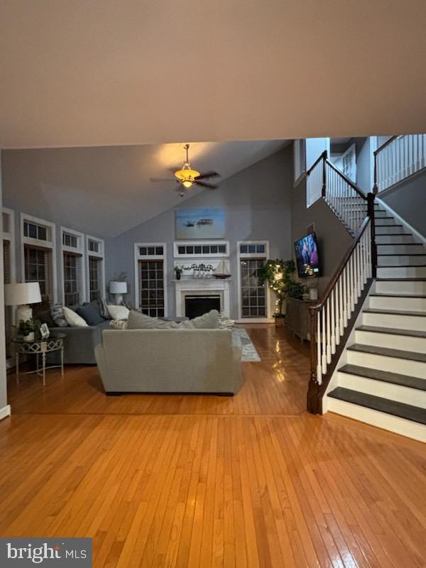 living area with stairway, ceiling fan, a fireplace, and light wood-style floors