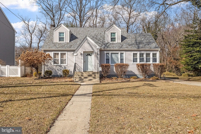 cape cod home featuring roof with shingles, fence, and a front lawn