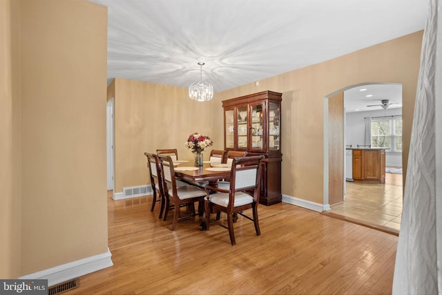 dining area featuring arched walkways, light wood-style flooring, visible vents, and baseboards