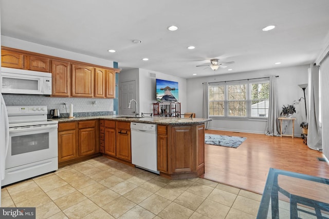 kitchen with a peninsula, white appliances, a sink, brown cabinets, and tasteful backsplash