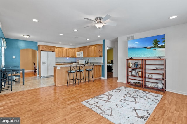 kitchen featuring arched walkways, light countertops, visible vents, white appliances, and a kitchen bar