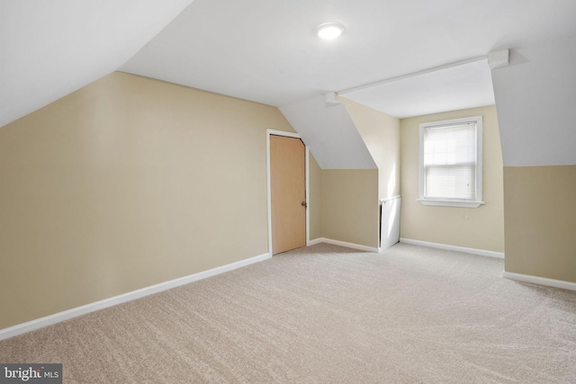 additional living space with vaulted ceiling, light colored carpet, and baseboards