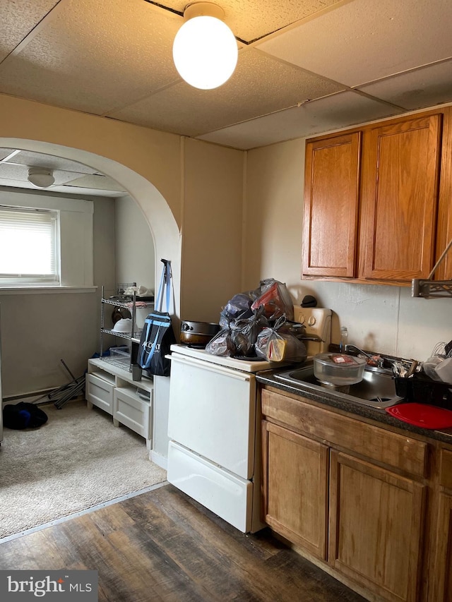 kitchen with brown cabinets, dark countertops, stove, dark wood-type flooring, and a drop ceiling