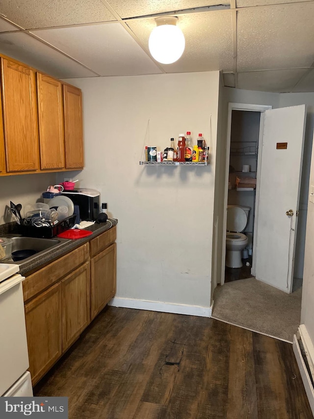 kitchen with a drop ceiling, dark countertops, dark wood-style floors, a baseboard radiator, and brown cabinets