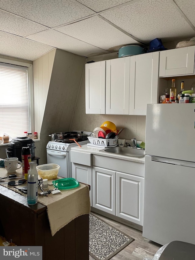 kitchen with white appliances, light countertops, a paneled ceiling, white cabinetry, and a sink