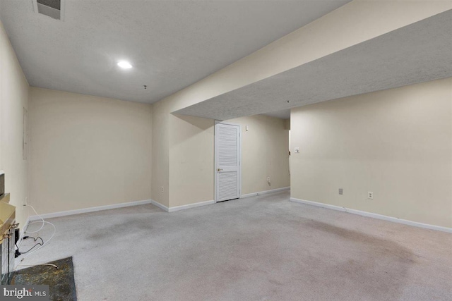 finished basement with carpet, visible vents, a textured ceiling, and baseboards