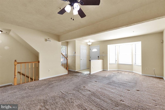 unfurnished living room with a textured ceiling, carpet flooring, a wealth of natural light, and baseboards