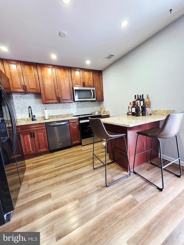 kitchen with stainless steel appliances, visible vents, light wood-style floors, and a kitchen breakfast bar