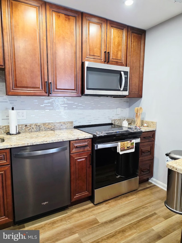 kitchen featuring light wood-style floors, light stone counters, stainless steel appliances, and decorative backsplash