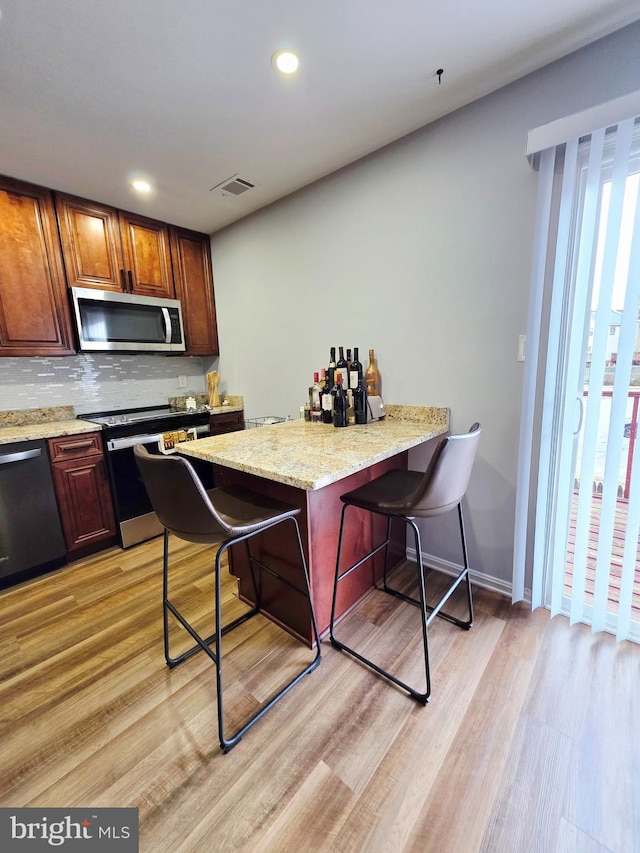 kitchen featuring a peninsula, appliances with stainless steel finishes, a kitchen bar, and visible vents