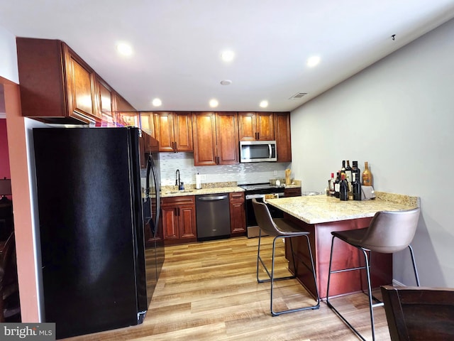 kitchen featuring light wood-style flooring, a peninsula, appliances with stainless steel finishes, tasteful backsplash, and a kitchen bar