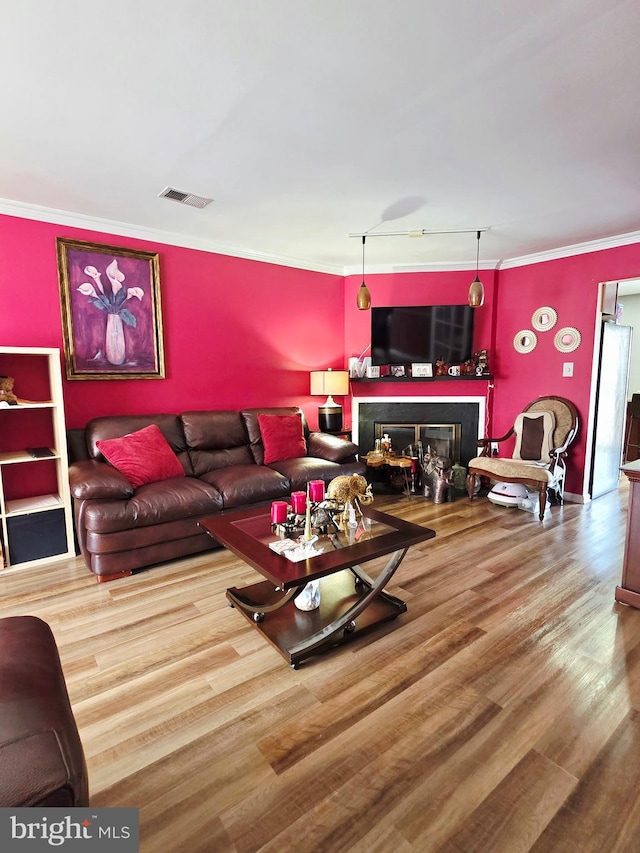 living room featuring ornamental molding, a glass covered fireplace, visible vents, and wood finished floors