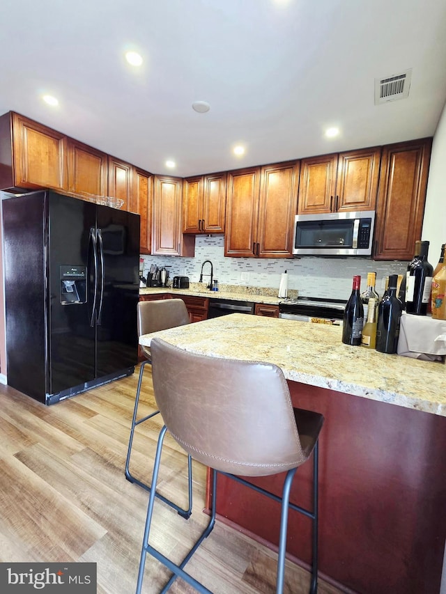 kitchen with visible vents, brown cabinetry, appliances with stainless steel finishes, light stone counters, and a sink