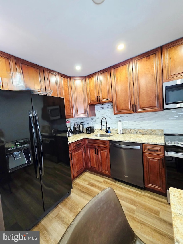 kitchen with a sink, appliances with stainless steel finishes, light wood-type flooring, light stone countertops, and tasteful backsplash