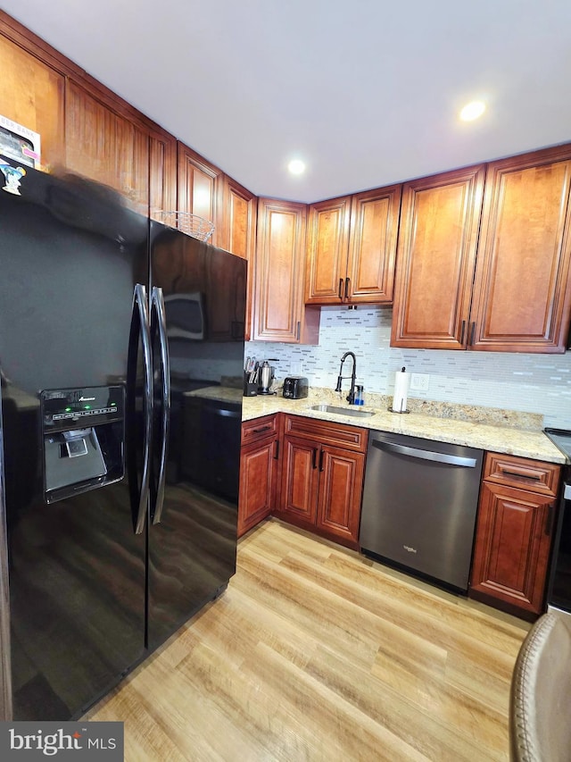 kitchen featuring dishwasher, black fridge with ice dispenser, light stone counters, light wood-type flooring, and a sink