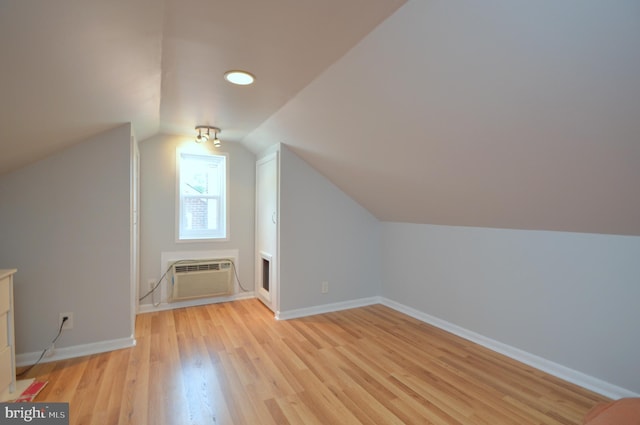 additional living space with an AC wall unit, vaulted ceiling, light wood-style flooring, and baseboards