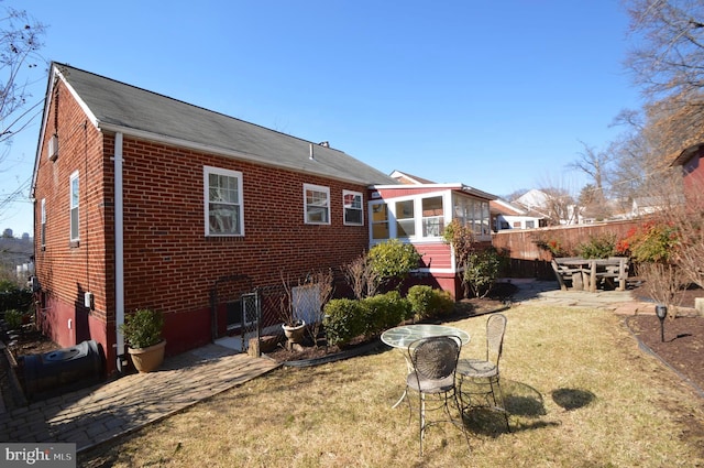 rear view of house with brick siding, fence, a sunroom, a yard, and a patio area