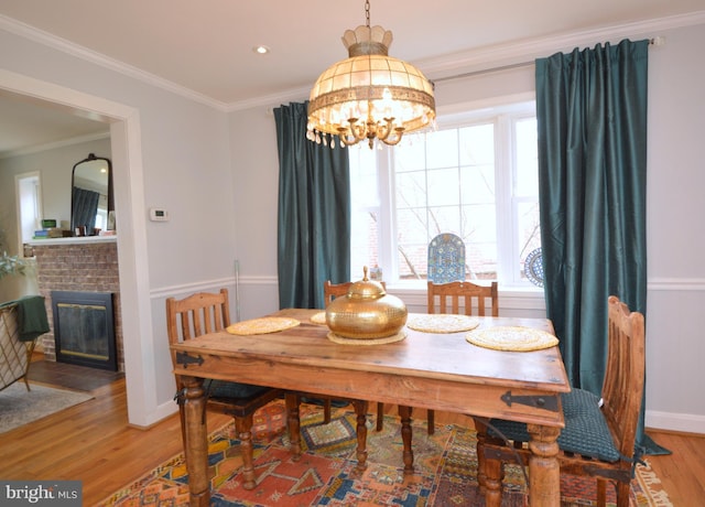 dining room featuring a notable chandelier, crown molding, a brick fireplace, wood finished floors, and baseboards