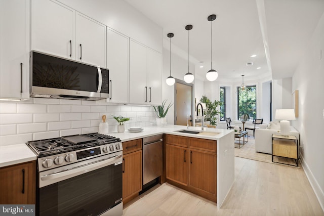 kitchen featuring a sink, white cabinets, light countertops, appliances with stainless steel finishes, and pendant lighting