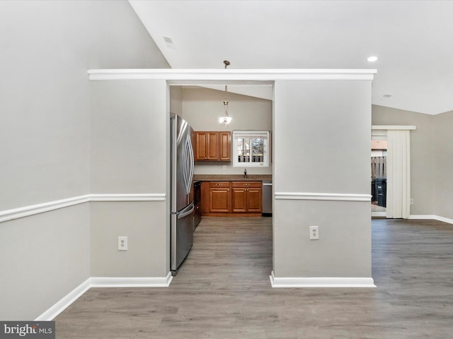 kitchen with decorative light fixtures, light wood-style flooring, appliances with stainless steel finishes, brown cabinetry, and vaulted ceiling