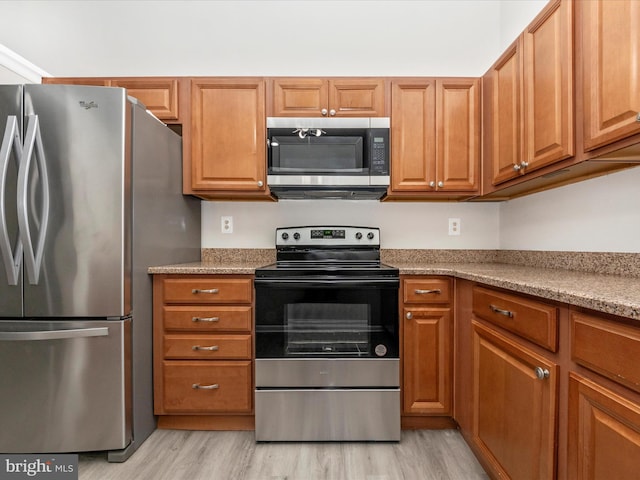 kitchen with light stone countertops, light wood-style flooring, stainless steel appliances, and brown cabinetry