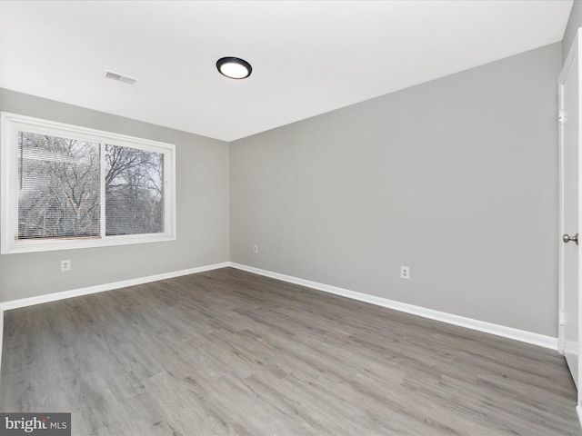 empty room with baseboards, visible vents, and wood finished floors