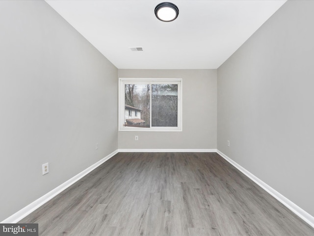 empty room featuring wood finished floors, visible vents, and baseboards