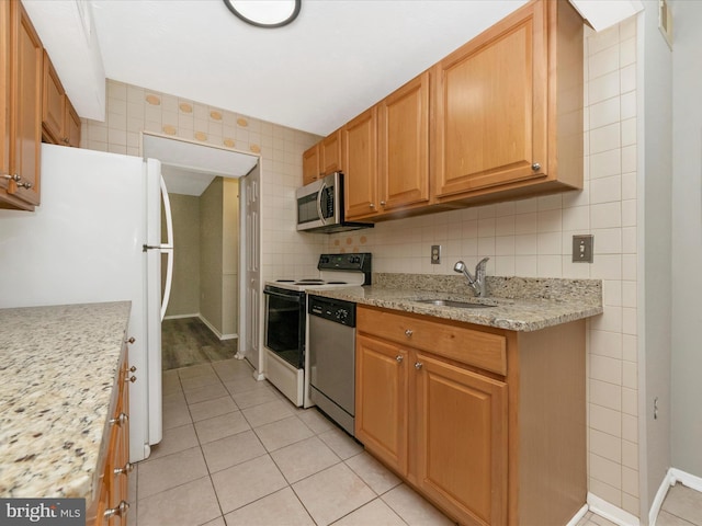 kitchen with light tile patterned floors, light stone counters, a sink, appliances with stainless steel finishes, and backsplash