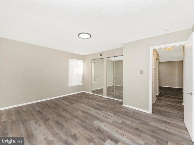 unfurnished bedroom featuring baseboards, wood finished floors, visible vents, and multiple closets