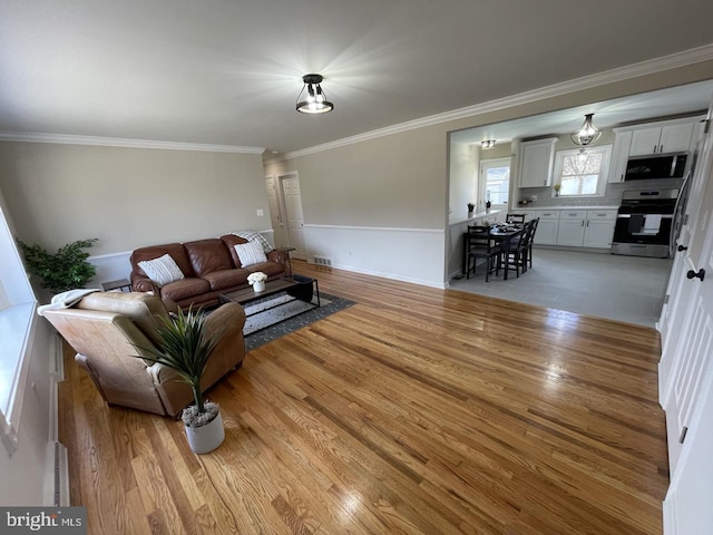 living area with light wood-type flooring, visible vents, and crown molding